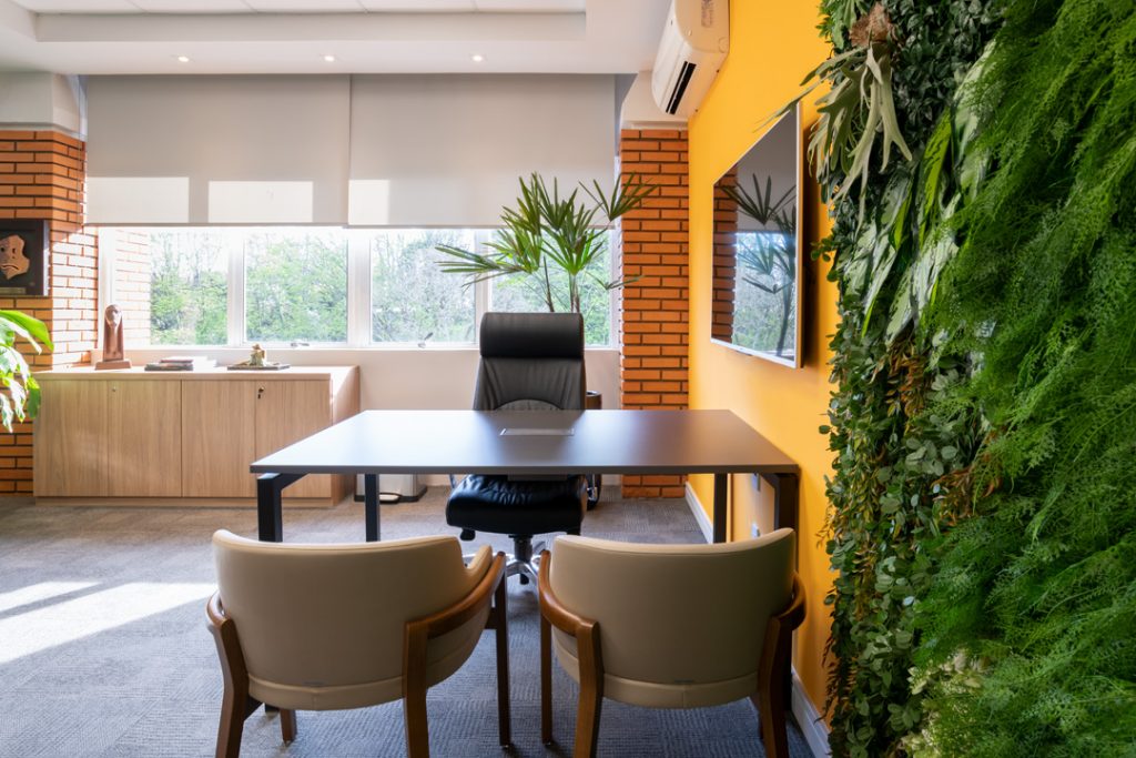 projetos de arquitetura corporativa com presença de plantas na parede direita, uma mesa de escritório com duas cadeiras e luz solar iluminando 