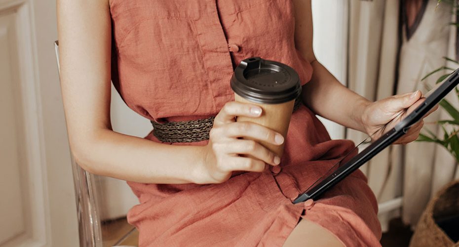 mulher sentada com copo de café na mão e na outra um tablet, exemplo de consumidor do futuro